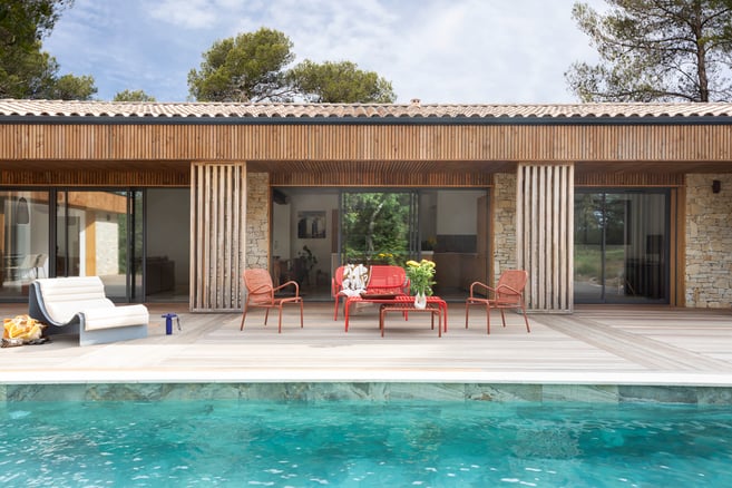 Maison avec terrasse lumineuse mélangée de pierres et de bois, avec piscine et salon de jardin. 