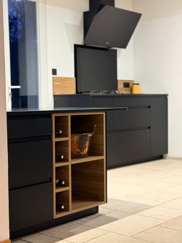  L'îlot s'ouvre côté salon sur un casier à bouteilles en chêne — fonctionnel, chaleureux, inattendu.