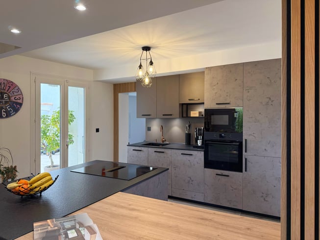 Cuisine ouverte à Vendargues avec îlot en granit noir, espace repas en bois et façades effet béton ciré.