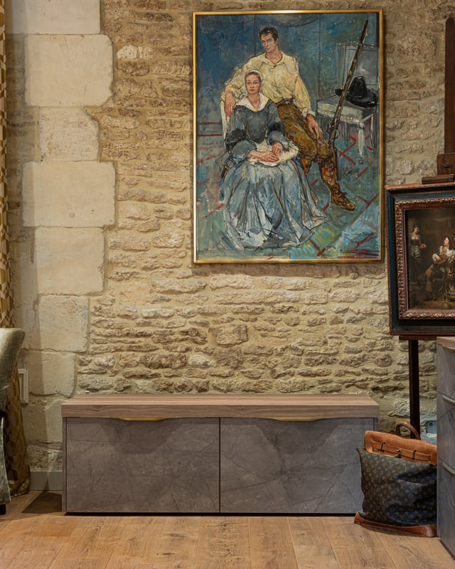 Meuble bas sur mesure sous un tableau, adossé à un mur en pierre.