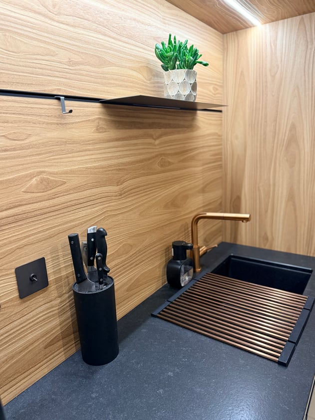 Chaque accessoire a été pensé jusqu'au bout — égouttoir et mitigeur aux touches cuivrées, plan de travail en pierre naturelle, matières nobles sur fond de chêne Okobo.