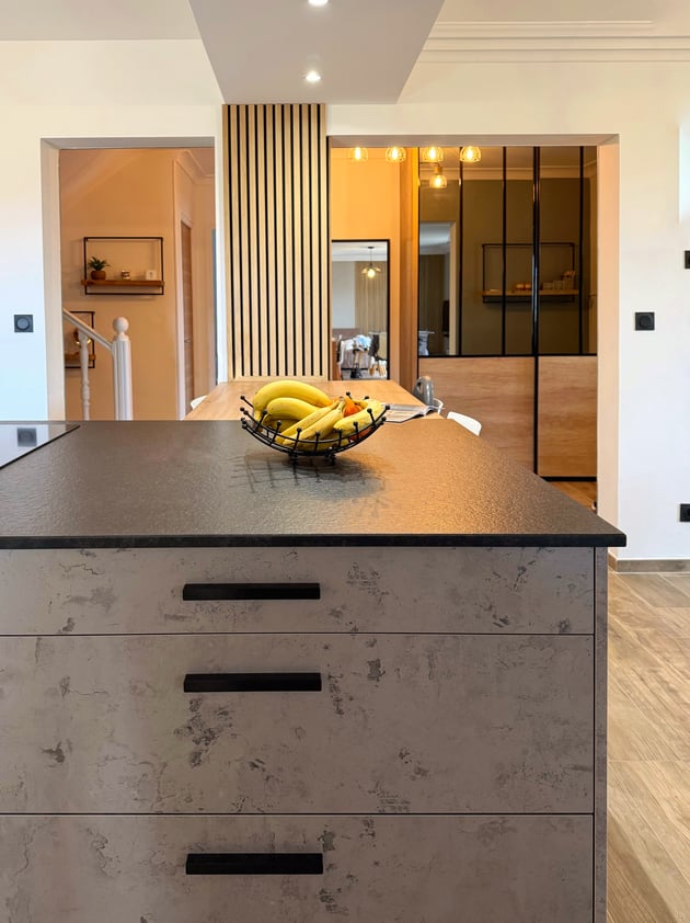 Îlot central de cuisine à Vendargues avec façades effet béton ciré, plan de travail en granit noir et tasseaux de bois.