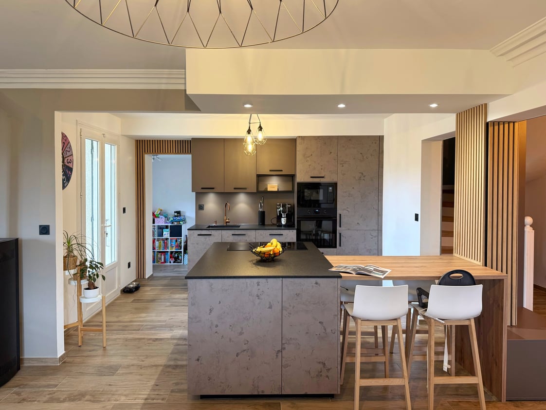 Cuisine familiale ouverte à Vendargues avec îlot central, coin repas en bois, façades effet béton ciré et plan de travail en granit noir.