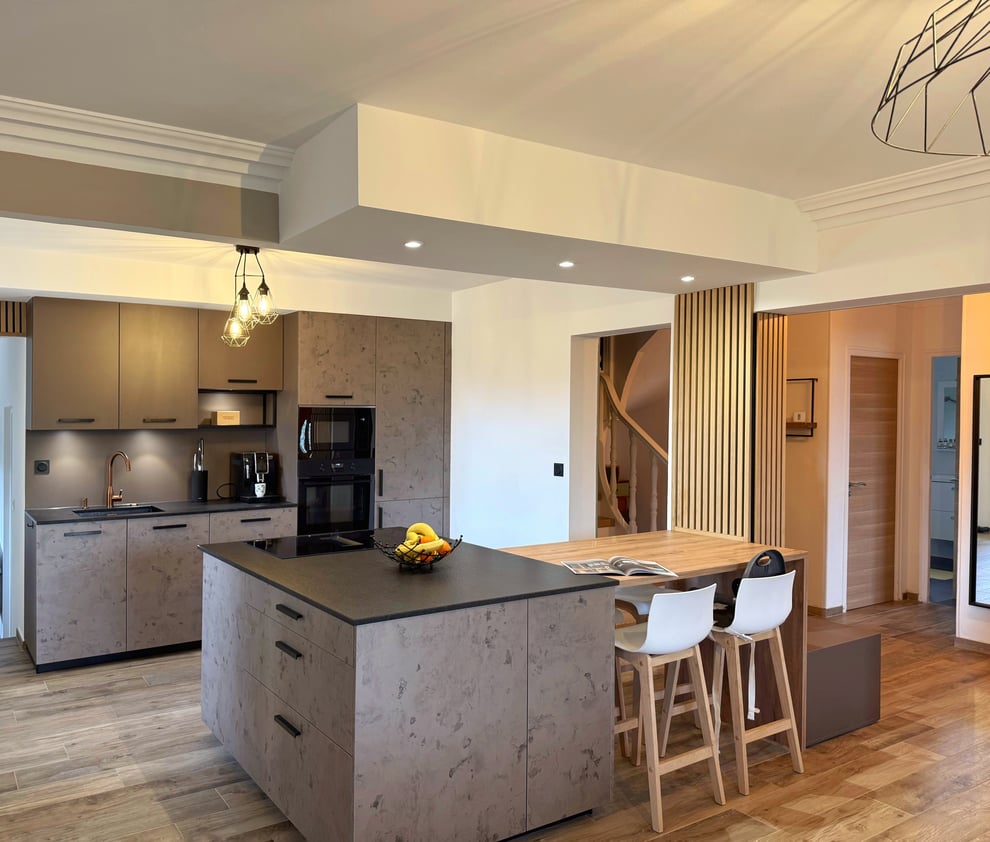 Cuisine ouverte à Vendargues avec îlot central, coin repas en bois, façades effet béton ciré et poteau habillé de tasseaux de bois.