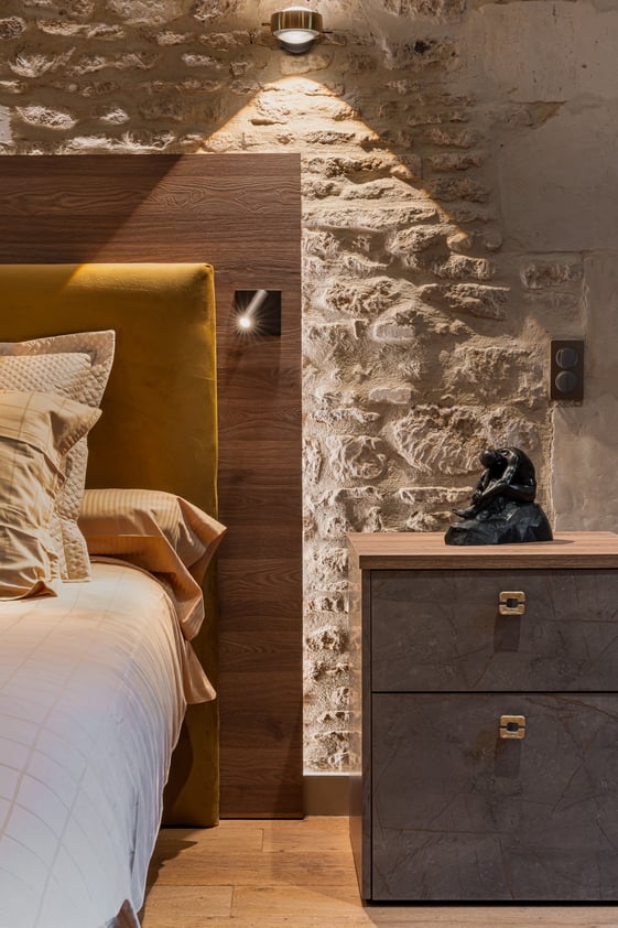 Tête de lit et chevet sur mesure dans une chambre de caractère aux murs en pierre.