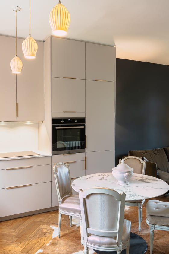 Cuisine aux façades claires et coin repas avec table ronde, chaises de style et suspensions lumineuses. Cuisine aux façades claires et coin repas avec table ronde, chaises de style et suspensions lumineuses.
