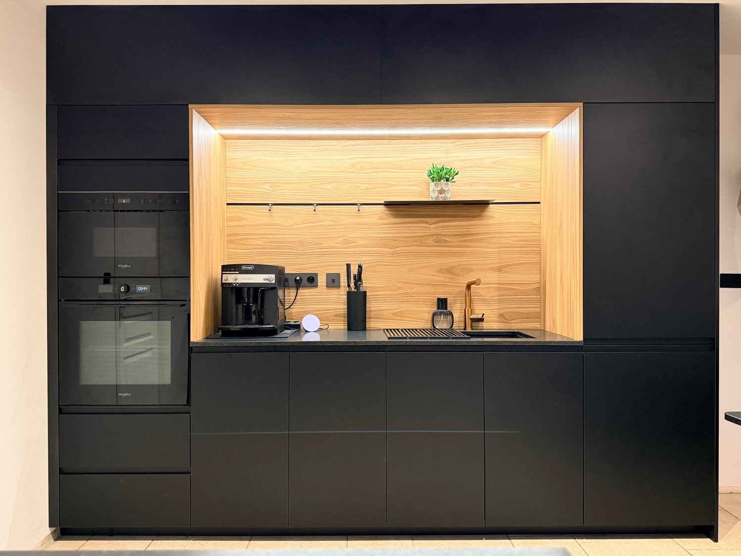 La niche en chêne Okobo, éclairée en LED, s'impose comme un écrin lumineux dans l'écrin noir mat.