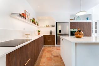 Cuisine sur mesure en noyer rainuré avec îlot central en quartz blanc, éléments en bâti et ambiance inspirée des maisons du Sud Cuisine sur mesure en noyer rainuré avec îlot central en quartz blanc, éléments en bâti et ambiance inspirée des maisons du Sud