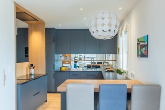 Profonde et lumineuse, la pièce offre de nombreux rangements facilement accessibles. La crédence en verre coupée par une étagère en bois reflète élégamment la pièce.