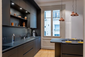 Entièrement habillé, le mur du fond se compose d'un linéaire de meubles bas, d'un jeu de 2 étagères centrales que viennent entourer 2 meubles hauts à droite et à gauche relié par un bandeau où sont insérés les spots lumineux.  