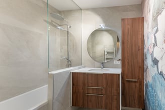 Un meuble vasque rehaussé d'un miroir arrondi et une colonne optimise l'espace de cette sall-de-bains.