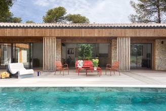 Maison avec terrasse lumineuse mélangée de pierres et de bois, avec piscine et salon de jardin. 