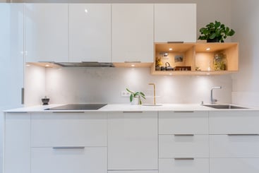 Blanche pour plus de lumière et quelques touches de bois pour apporter de la chaleur et du confort, cette cuisine très fonctionnelle est à la fois ouverte sur l'espace salle-à-manger tout en étant cachée. Aucun appareil électro-ménager ne se laisse voir par l'ouverture ! 