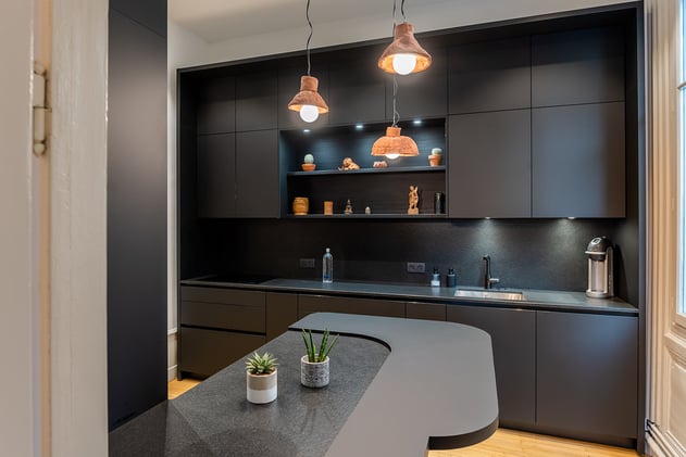 Entièrement habillé, le mur du fond se compose d'un linéaire de meubles bas, d'un jeu de 2 étagères centrales que viennent entourer 2 meubles hauts à droite et à gauche relié par un bandeau où sont insérés les spots lumineux.  