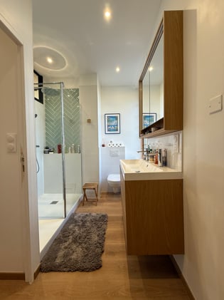 La salle de bain parentale, pensée dans la longueur — douche italienne en chevron vert sauge, meuble chêne miel, fonctionnelle et élégante.