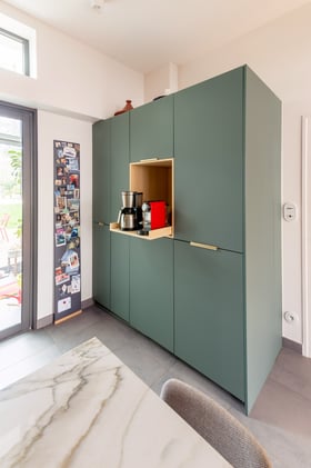 Séparée de la salle-à-manger par une verrière, la cuisine ne comporte que des meubles bas dans sa partie visible depuis celle-ci.