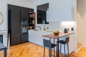 Chic et élégante, cette cuisine ouverte offre tous les rangements nécessaires tout en s'intégrant parfaitement au milieu des cheminées, parquet, moulures et autres détails très haussmanniens. 