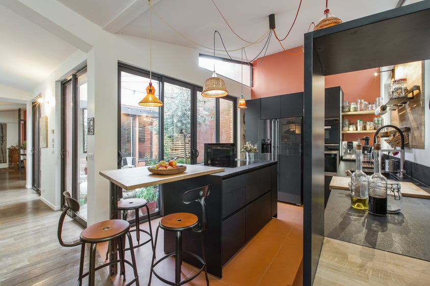 Vue d'ensemble sur cette cuisine fonctionnelle, lumineuse grâce au patio et à plusieurs fenêtres qui donnent sur une cour .